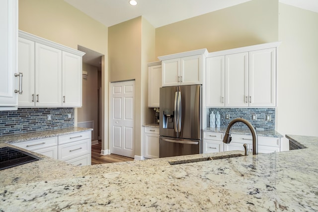 kitchen featuring white cabinetry, stainless steel fridge with ice dispenser, sink, and light stone countertops