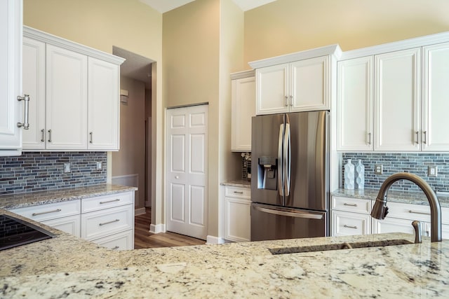 kitchen with white cabinetry, sink, light stone countertops, and stainless steel refrigerator with ice dispenser