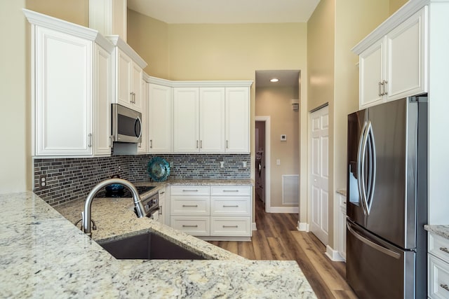 kitchen with white cabinets, sink, light stone countertops, appliances with stainless steel finishes, and tasteful backsplash