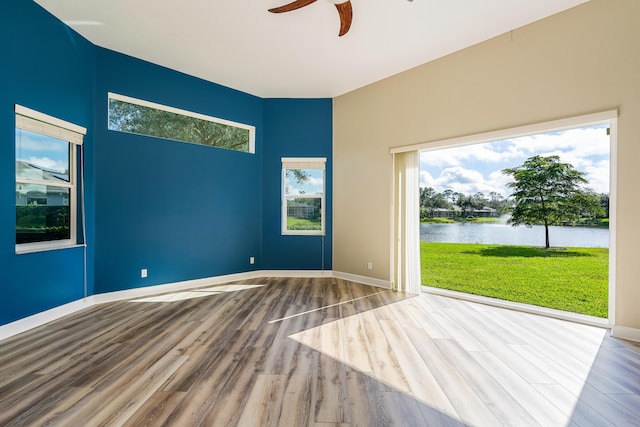 unfurnished room with ceiling fan, hardwood / wood-style floors, and a water view