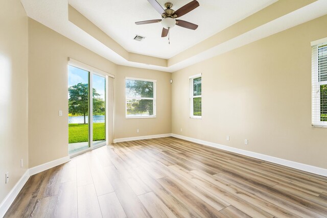 empty room with ceiling fan, light wood-type flooring, and a tray ceiling