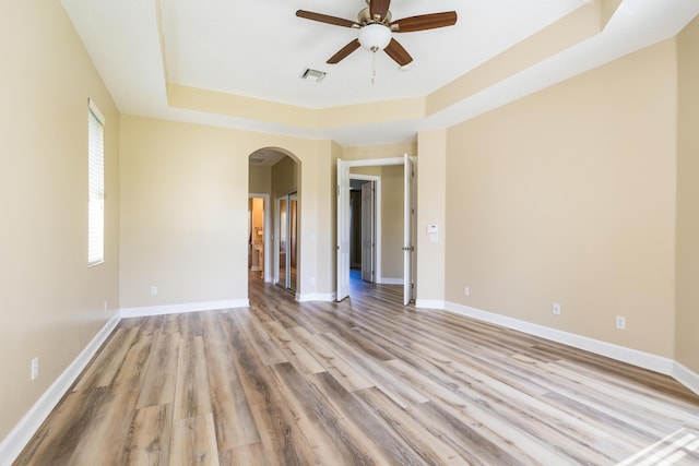 spare room with light wood-type flooring, a raised ceiling, and ceiling fan