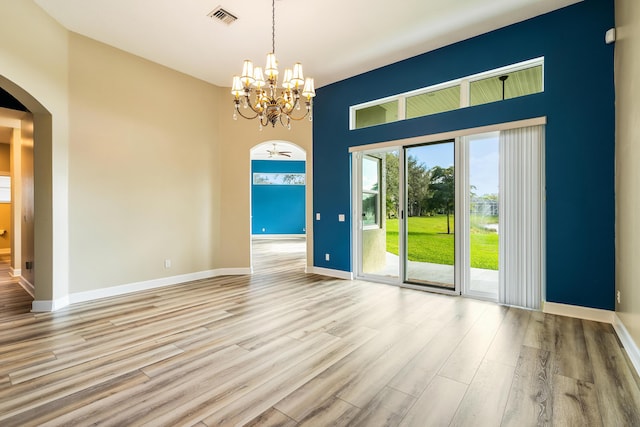 spare room with a towering ceiling, light hardwood / wood-style flooring, and a chandelier