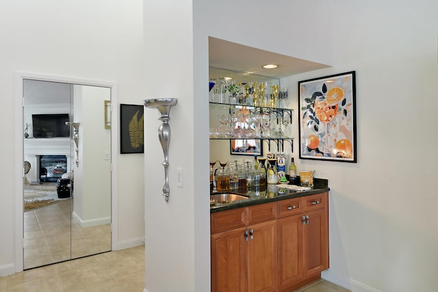 bar featuring light tile patterned flooring, dark stone countertops, and sink