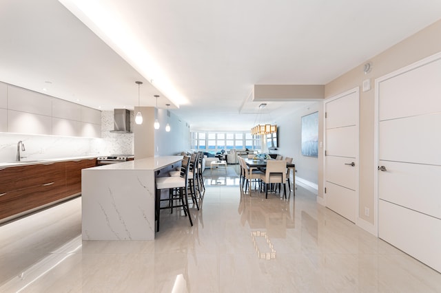 kitchen featuring hanging light fixtures, sink, backsplash, wall chimney range hood, and a spacious island