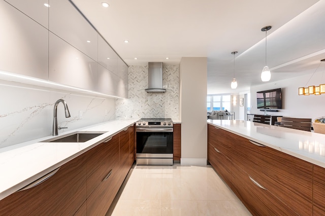 kitchen with light stone counters, sink, decorative light fixtures, wall chimney range hood, and stainless steel range oven