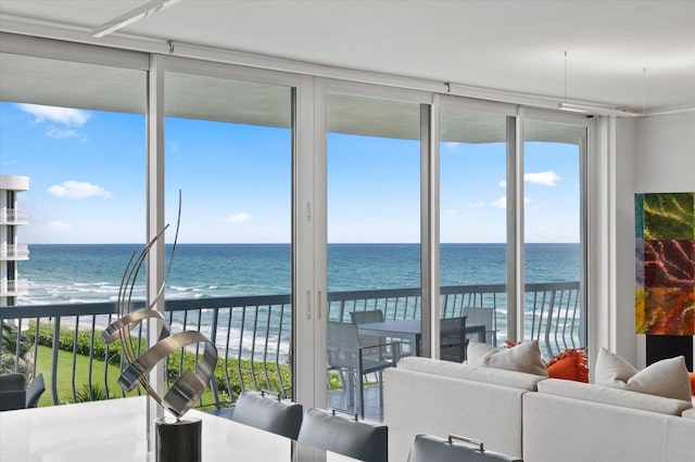 living room with expansive windows, a water view, and a view of the beach