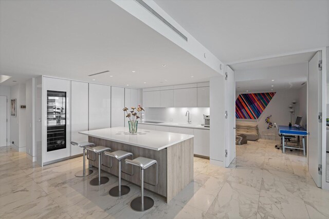 kitchen featuring a breakfast bar, wine cooler, a center island, sink, and white cabinets