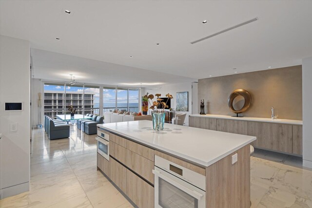 kitchen featuring a wall of windows, white oven, stainless steel oven, light brown cabinetry, and a center island