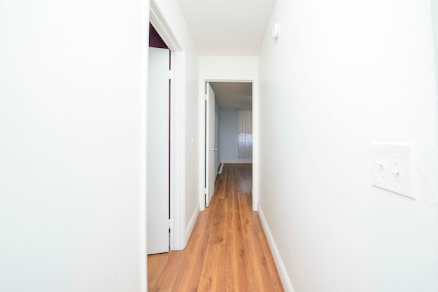 corridor with a textured ceiling and light wood-type flooring