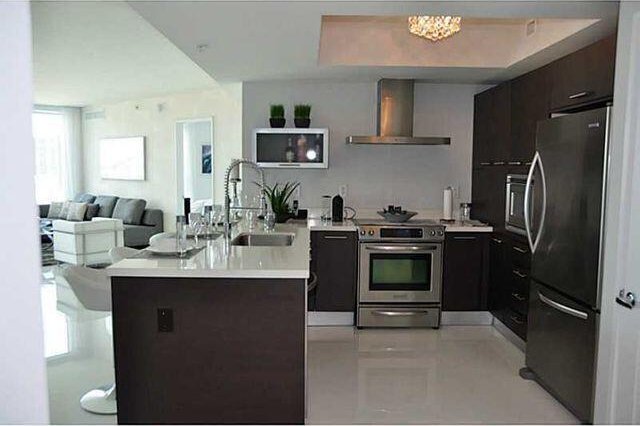 kitchen featuring appliances with stainless steel finishes, dark brown cabinets, sink, and wall chimney range hood