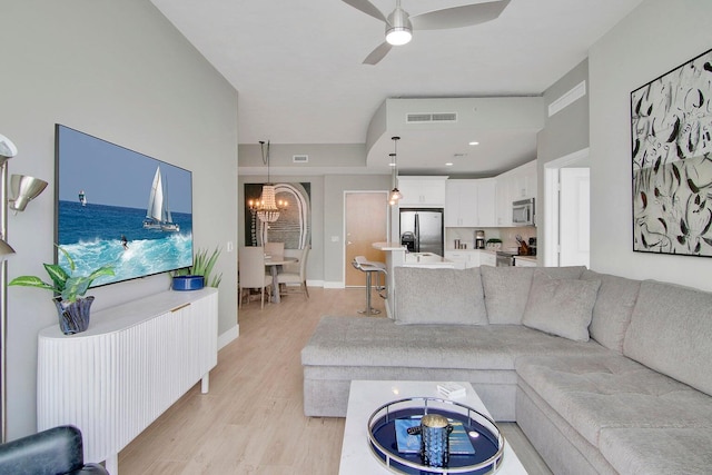 living room featuring ceiling fan with notable chandelier and light hardwood / wood-style floors