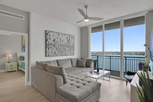 living room featuring ceiling fan, light hardwood / wood-style floors, a water view, and expansive windows