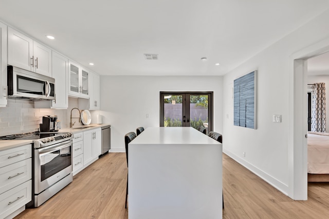 kitchen with light wood-type flooring, a center island, sink, white cabinetry, and appliances with stainless steel finishes