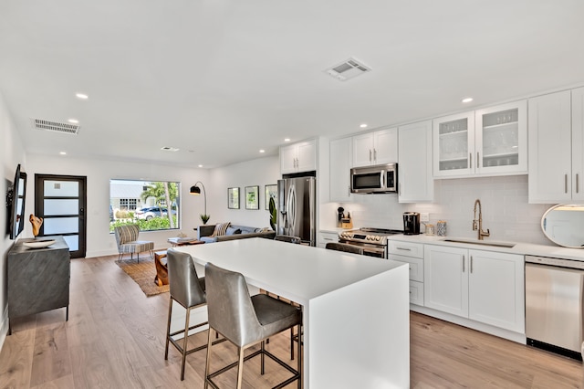 kitchen with a kitchen bar, stainless steel appliances, sink, and white cabinetry