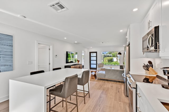 kitchen with light wood-type flooring, white cabinets, a kitchen island, a kitchen breakfast bar, and appliances with stainless steel finishes