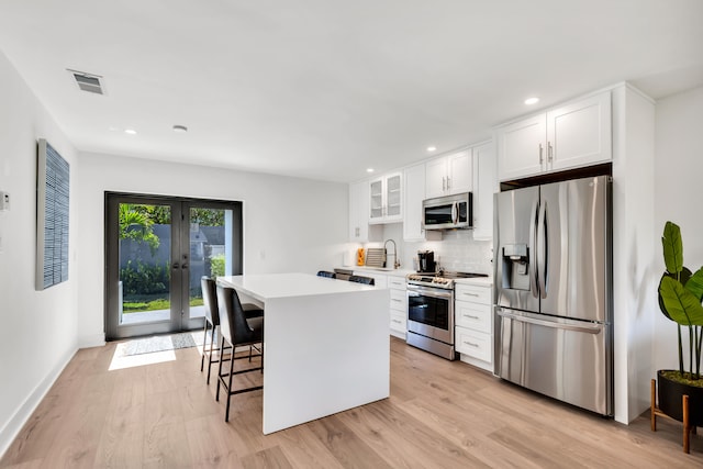 kitchen featuring a kitchen island, white cabinetry, stainless steel appliances, a kitchen breakfast bar, and light hardwood / wood-style floors