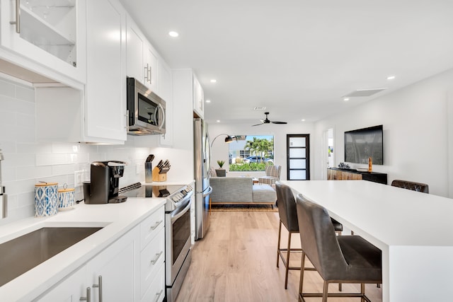 kitchen featuring tasteful backsplash, white cabinets, stainless steel appliances, a kitchen bar, and light hardwood / wood-style flooring