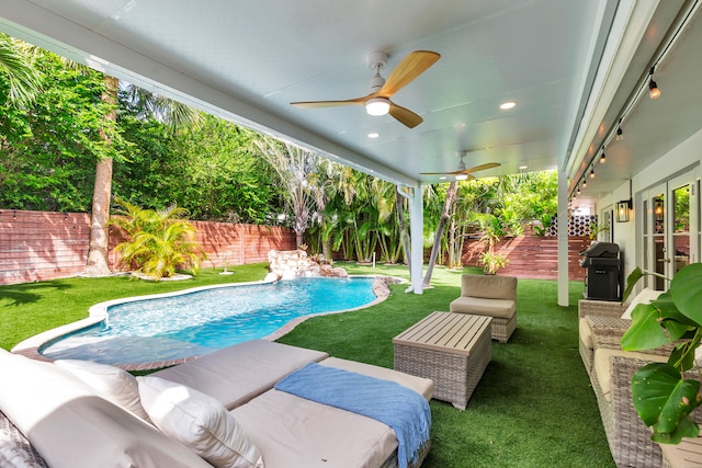 view of pool featuring ceiling fan, pool water feature, an outdoor living space, and a lawn