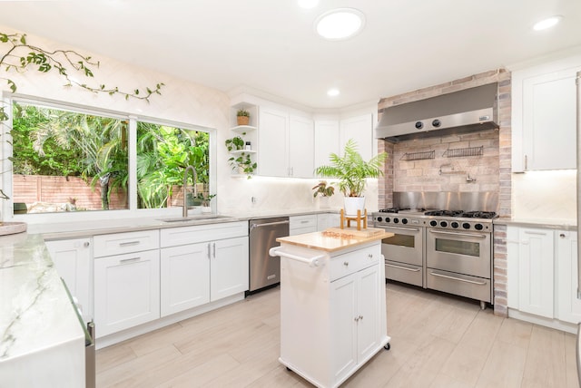 kitchen with backsplash, sink, light stone countertops, stainless steel appliances, and wall chimney exhaust hood