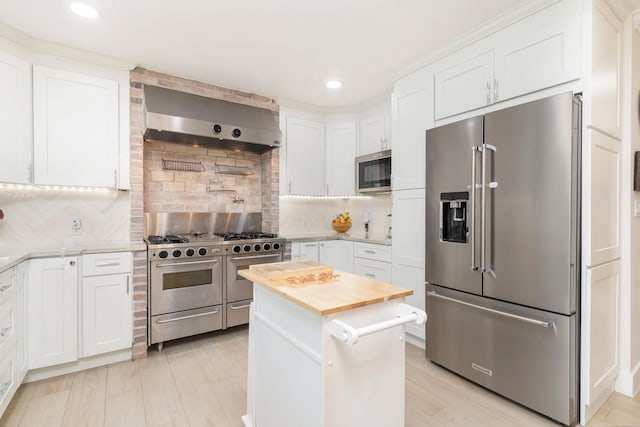 kitchen with white cabinetry, premium appliances, wall chimney exhaust hood, and tasteful backsplash