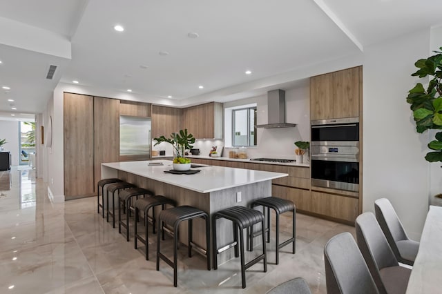 kitchen with wall chimney exhaust hood, a wealth of natural light, a kitchen breakfast bar, and a large island