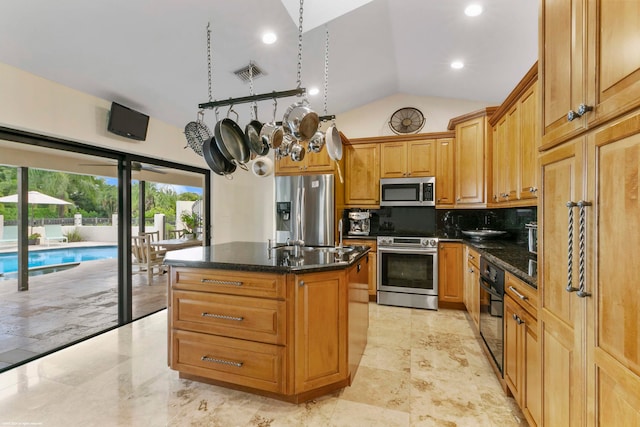 kitchen featuring appliances with stainless steel finishes, dark stone counters, an island with sink, and tasteful backsplash