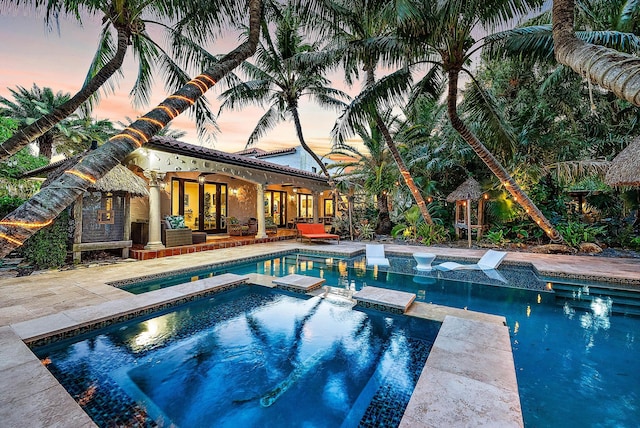 pool at dusk with an in ground hot tub and a patio area