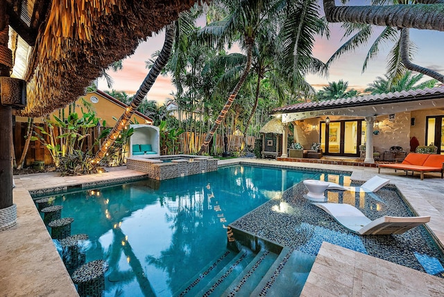 pool at dusk featuring an in ground hot tub and a patio area