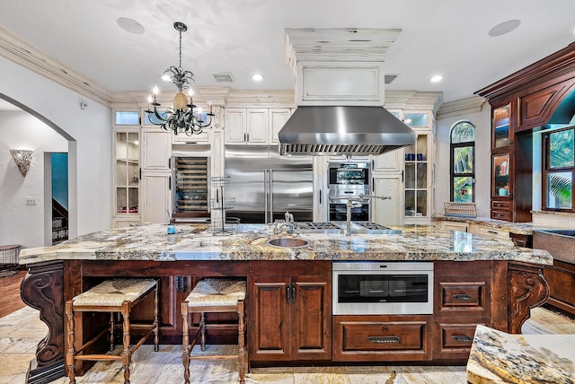 kitchen featuring stainless steel appliances, hanging light fixtures, a large island with sink, and crown molding