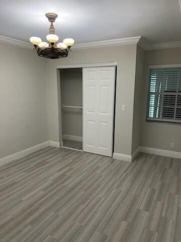 unfurnished bedroom featuring a notable chandelier, hardwood / wood-style flooring, a closet, and ornamental molding