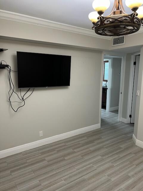 unfurnished room featuring light hardwood / wood-style floors, ornamental molding, and an inviting chandelier