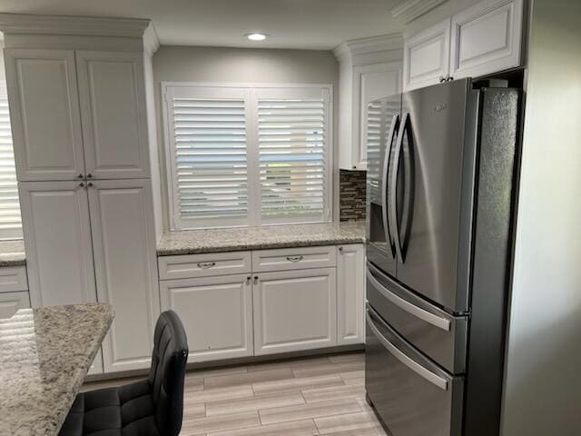 kitchen featuring white cabinets, stainless steel refrigerator with ice dispenser, light stone countertops, and light hardwood / wood-style floors