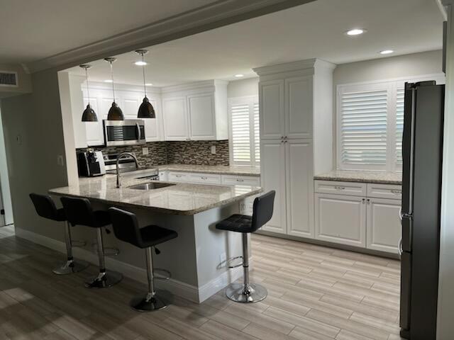 kitchen with a breakfast bar, white cabinets, light stone countertops, pendant lighting, and fridge