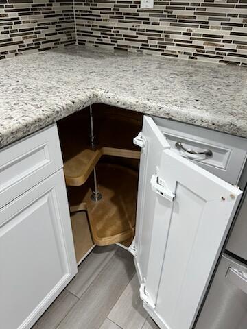 details featuring backsplash, light stone counters, and white cabinets