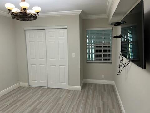 unfurnished bedroom featuring an inviting chandelier, a closet, crown molding, and light hardwood / wood-style floors