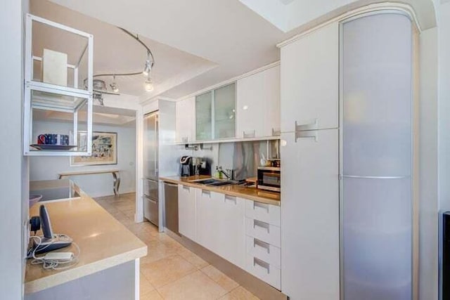 kitchen with appliances with stainless steel finishes, light tile patterned flooring, sink, a tray ceiling, and white cabinetry