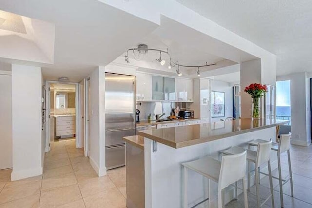 kitchen featuring stainless steel appliances, backsplash, a kitchen bar, light tile patterned floors, and white cabinets