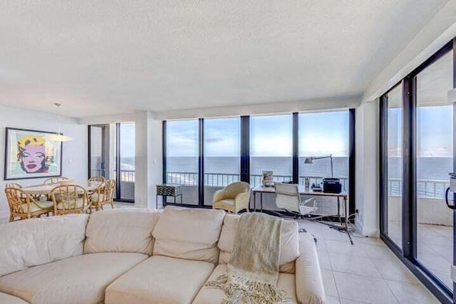 living room with a wall of windows, a textured ceiling, a water view, and light tile patterned floors