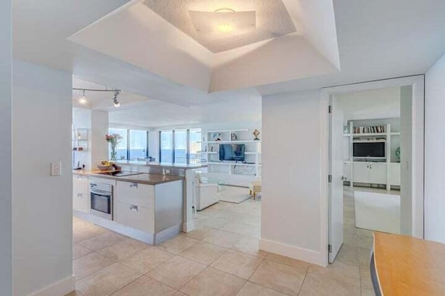 kitchen featuring oven, white cabinetry, light tile patterned flooring, and a tray ceiling