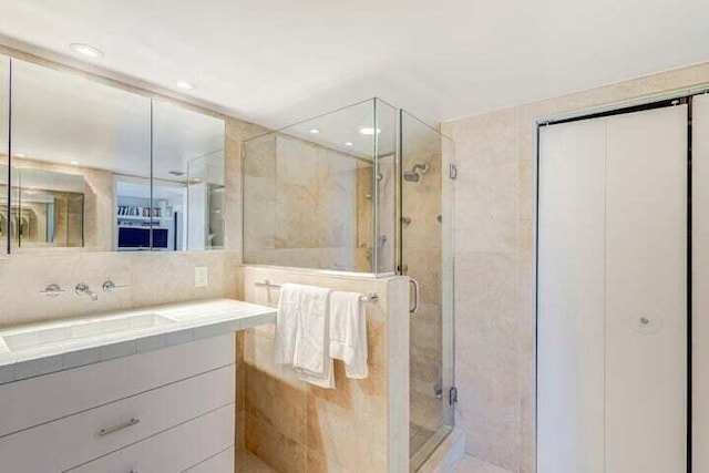 bathroom with tile walls, vanity, and a shower with shower door