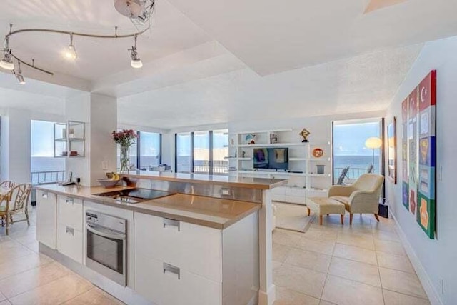 kitchen with oven, white cabinets, light tile patterned floors, black electric cooktop, and a water view