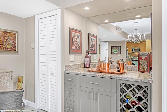 bar with pendant lighting, light stone counters, a notable chandelier, gray cabinetry, and stainless steel appliances