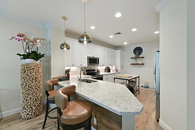 kitchen with appliances with stainless steel finishes, kitchen peninsula, white cabinetry, and light hardwood / wood-style flooring