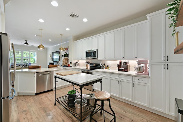 kitchen with hanging light fixtures, white cabinets, kitchen peninsula, stainless steel appliances, and light wood-type flooring