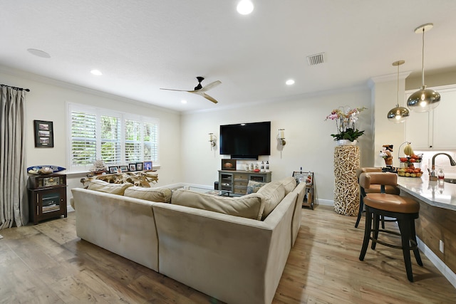 living room featuring light wood-type flooring, crown molding, sink, and ceiling fan