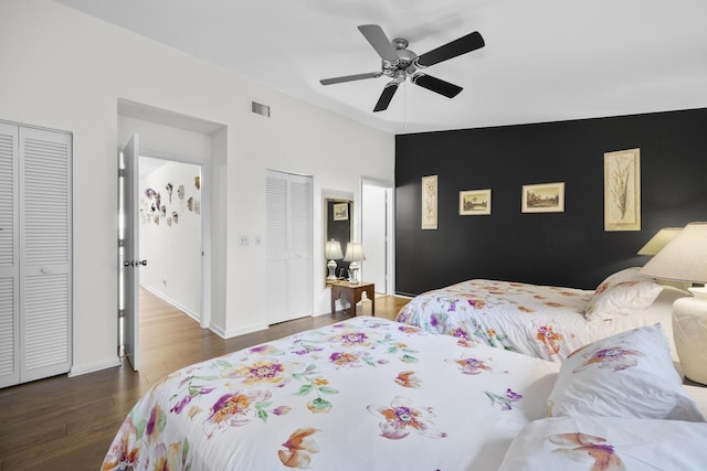 bedroom with two closets, dark hardwood / wood-style floors, and ceiling fan