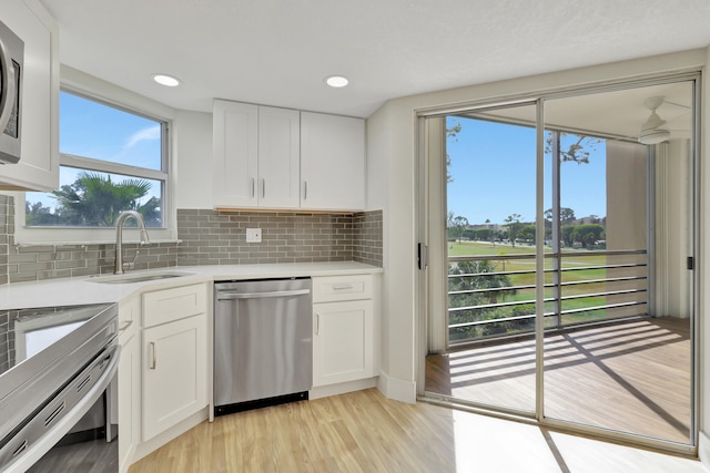 kitchen with appliances with stainless steel finishes, white cabinets, backsplash, light wood-type flooring, and sink