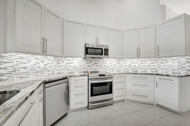 kitchen with white cabinetry, appliances with stainless steel finishes, light stone counters, and light tile patterned flooring