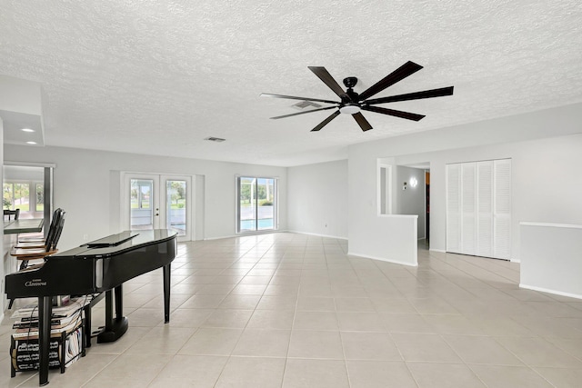 living area with a textured ceiling, light tile patterned flooring, visible vents, baseboards, and french doors